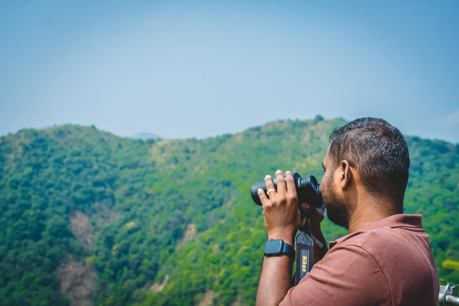 A birder scanning a forested hillside through binoculars